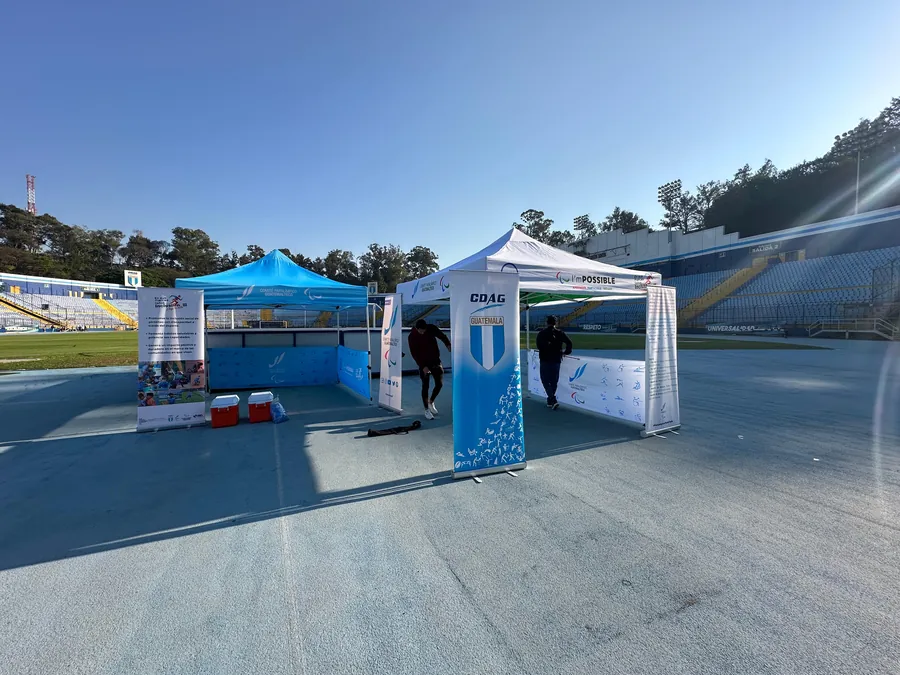 Dos toldos publicitarios de CDAG Guatemala y del Comité Paralímpico Guatemalteco con banderolas y paneles, montados en la pista de un estadio