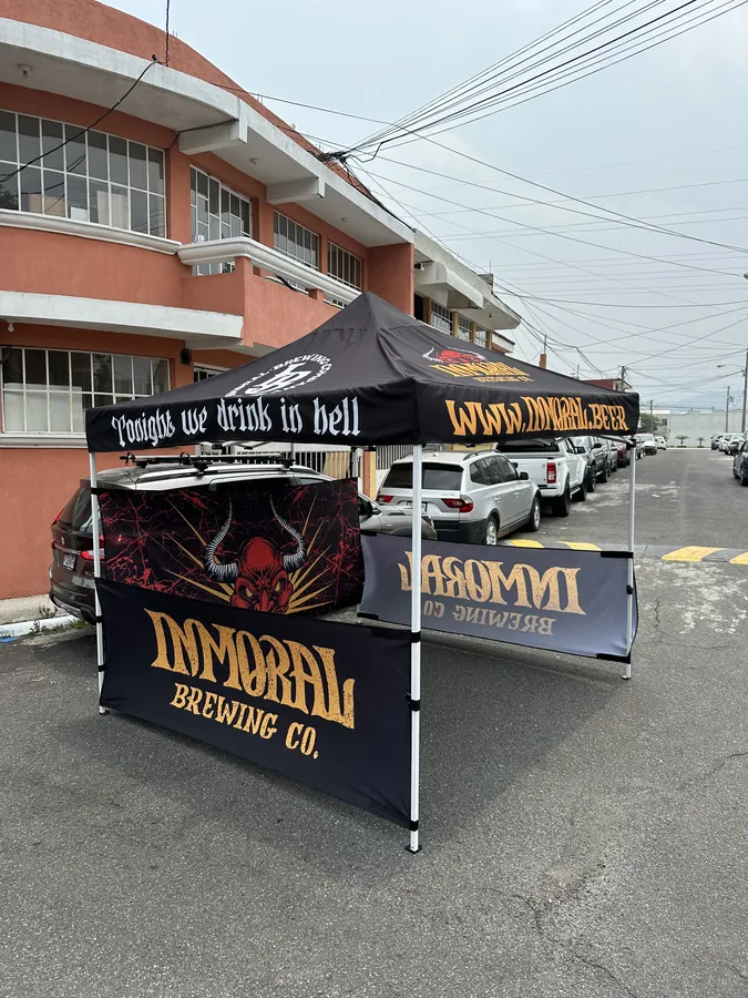 Toldo negro con faldón lateral impreso de Inmoral Brewing Co., montado en la calle