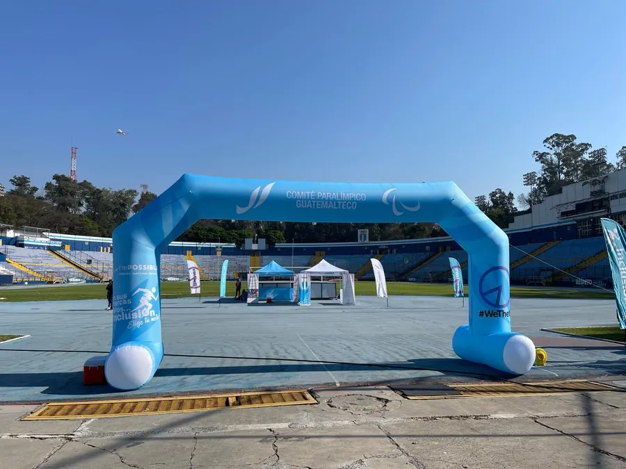 Arco inflable celeste del Comité Paralímpico Guatemalteco en la pista de un estadio, con toldos y banderolas al fondo