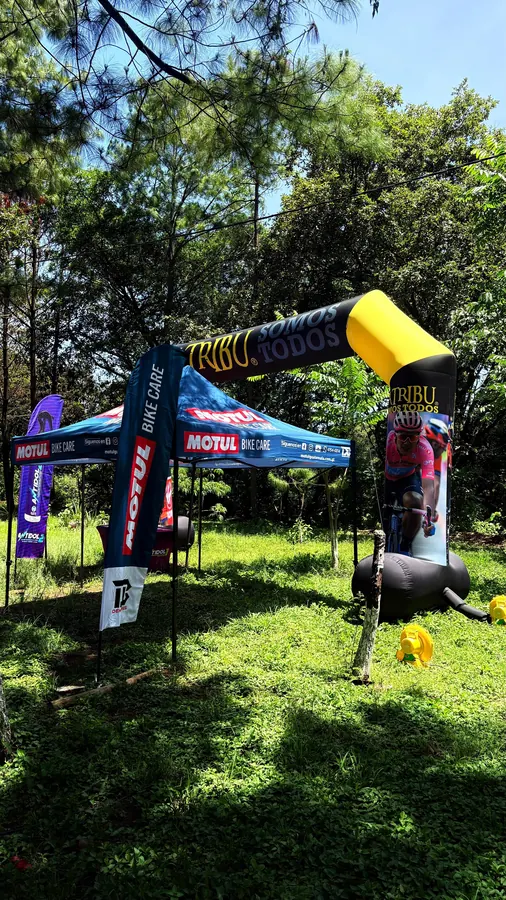 Arco inflable «La Tribu · Somos todos» y toldo de Motul Bike Care con banderolas, en un evento de ciclismo de montaña entre árboles